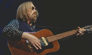 Tom Petty performs on stage, playing a guitar and singing