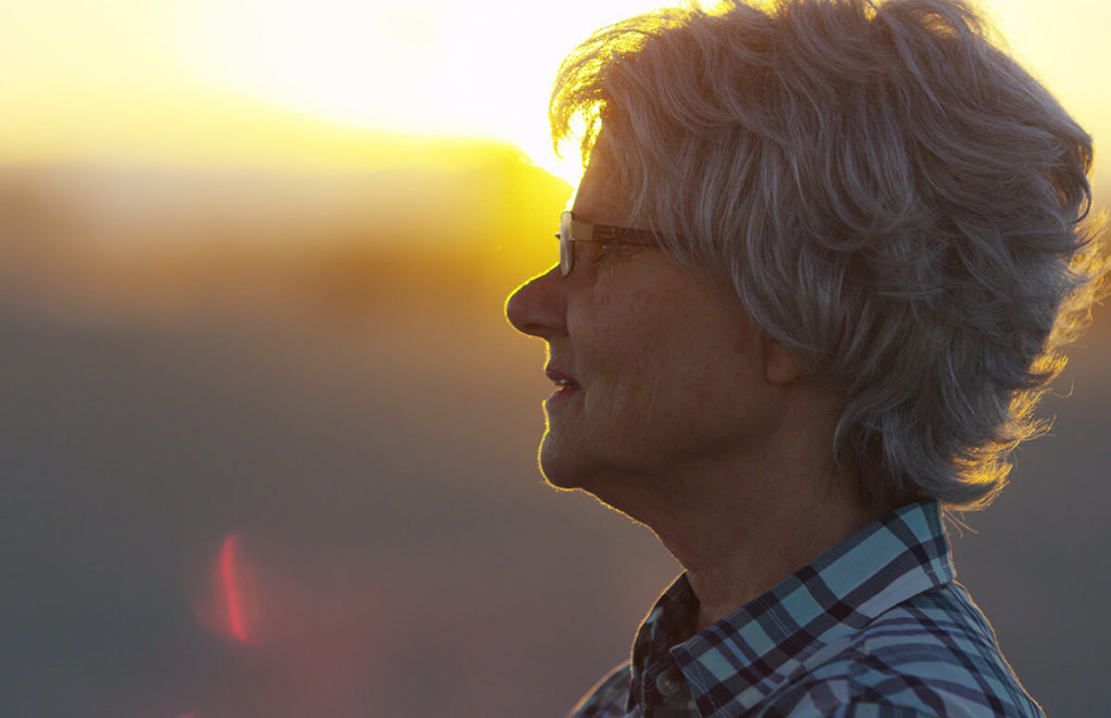 Senior woman gazes pensively into the distance while the sun sets behind her